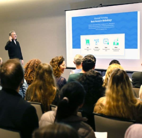 A speaker presenting to a seated audience in a lecture room.