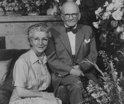 A family portrait: an elderly couple seated together among flowers.