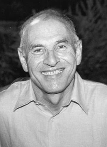 A smiling man in an open-necked shirt, photographed outdoors.