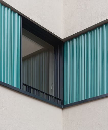 A corner window of a renovated apartment building with teal shutters.